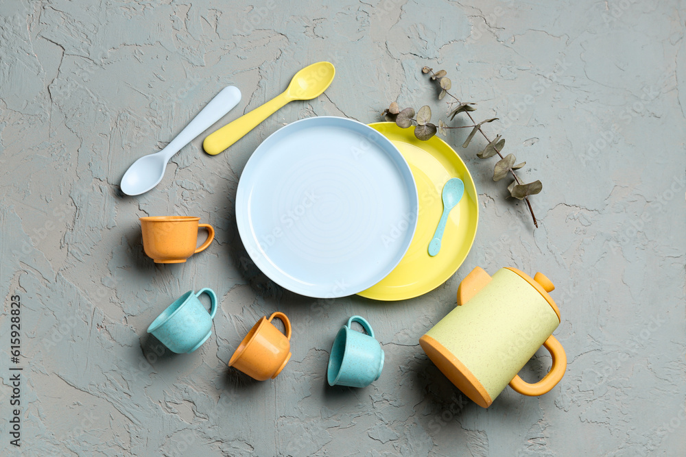 Teapot with cups, plates for baby and eucalyptus branch on grey background