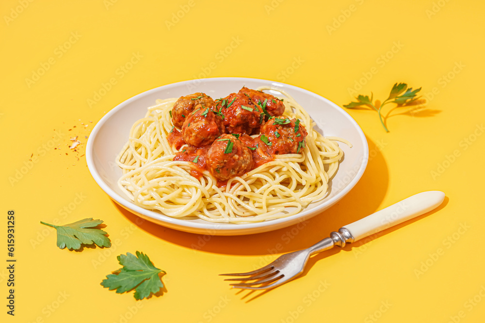 Plate of boiled pasta with tomato sauce and meat balls on yellow background