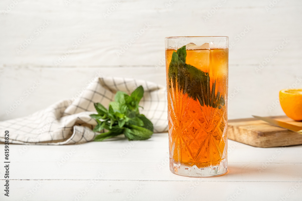 Glass of ice tea and board with orange on white wooden background