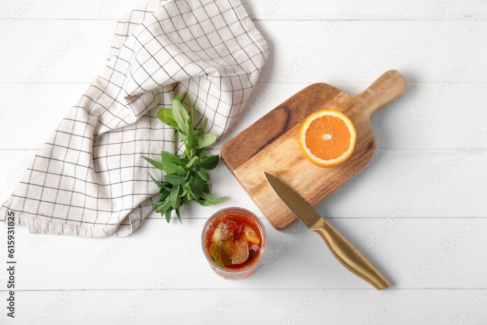 Glass of ice tea and board with orange on white wooden background