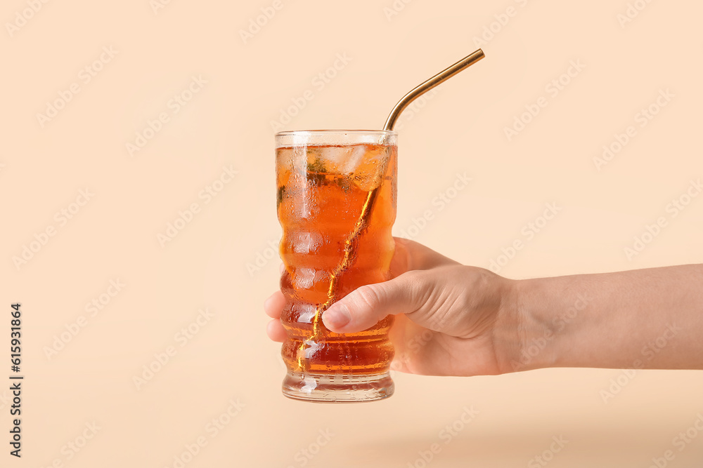 Female hand holding glass of ice tea on beige background