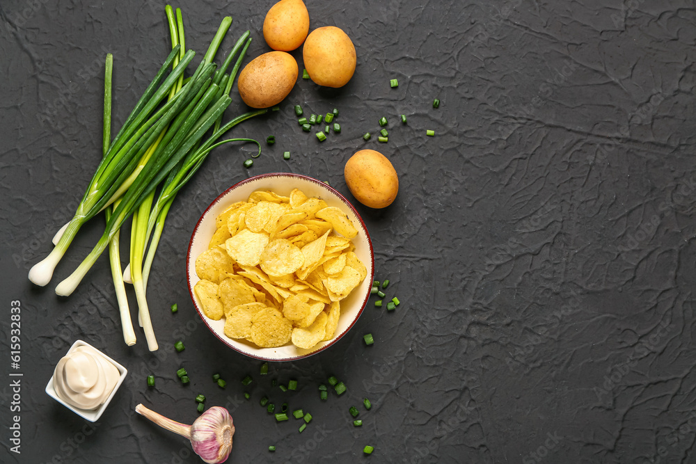 Bowl of tasty sour cream with green onion and potato chips on black background