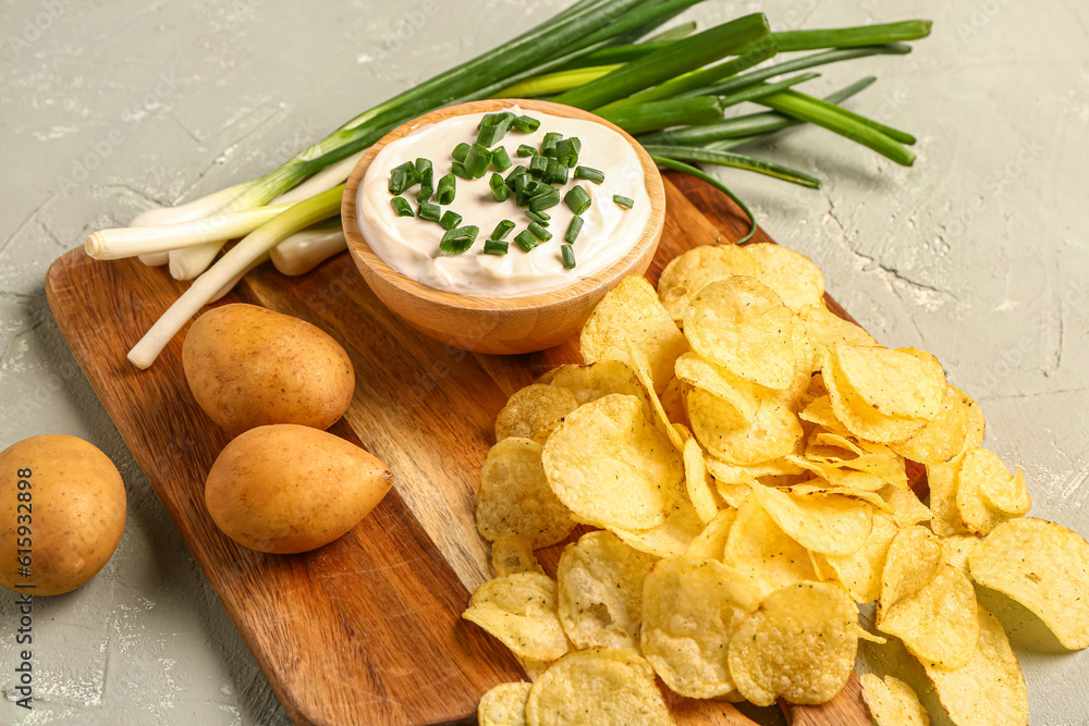 Bowl of tasty sour cream with sliced green onion and potato chips on grey background