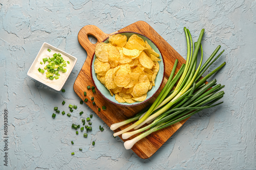 Bowl of tasty sour cream with sliced green onion and potato chips on blue background