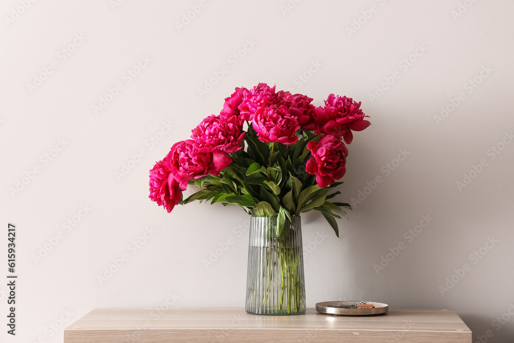 Vase of red peonies on dresser near light wall