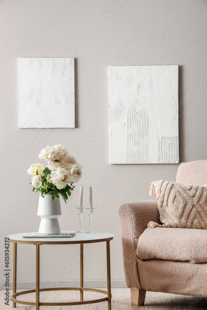 Vase of white peonies with coffee table and armchair near grey wall