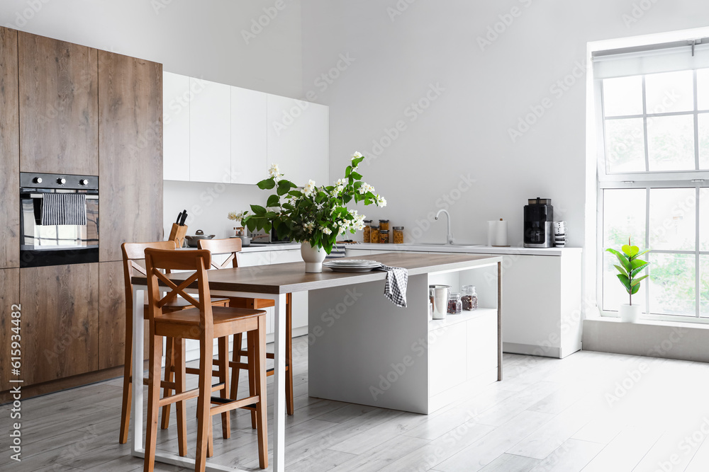 Interior of light kitchen decorated with blooming jasmine flowers in vase