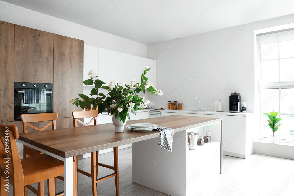 Interior of light kitchen decorated with blooming jasmine flowers in vase