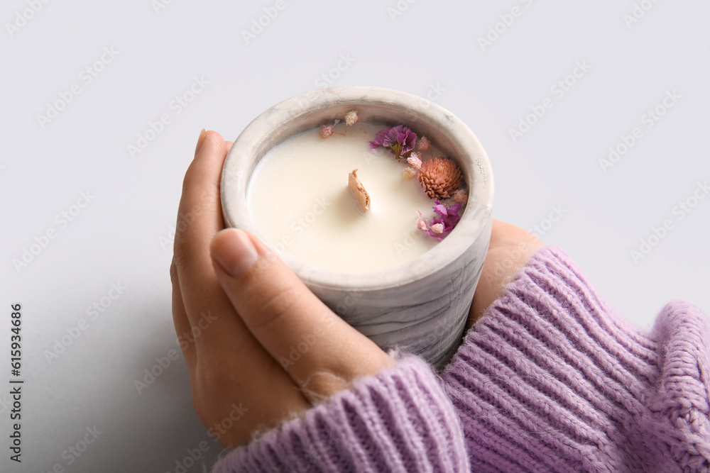 Female hands with candle and flowers on grey background, closeup