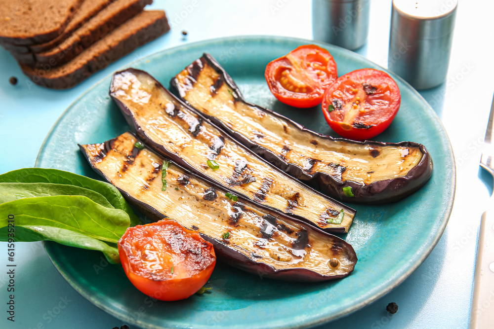 Plate with delicious grilled eggplants and tomatoes on light blue background