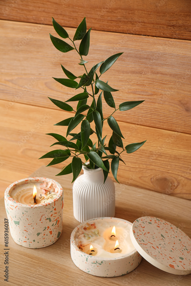 Beautiful branch and burning candles on table near wooden wall in room, closeup