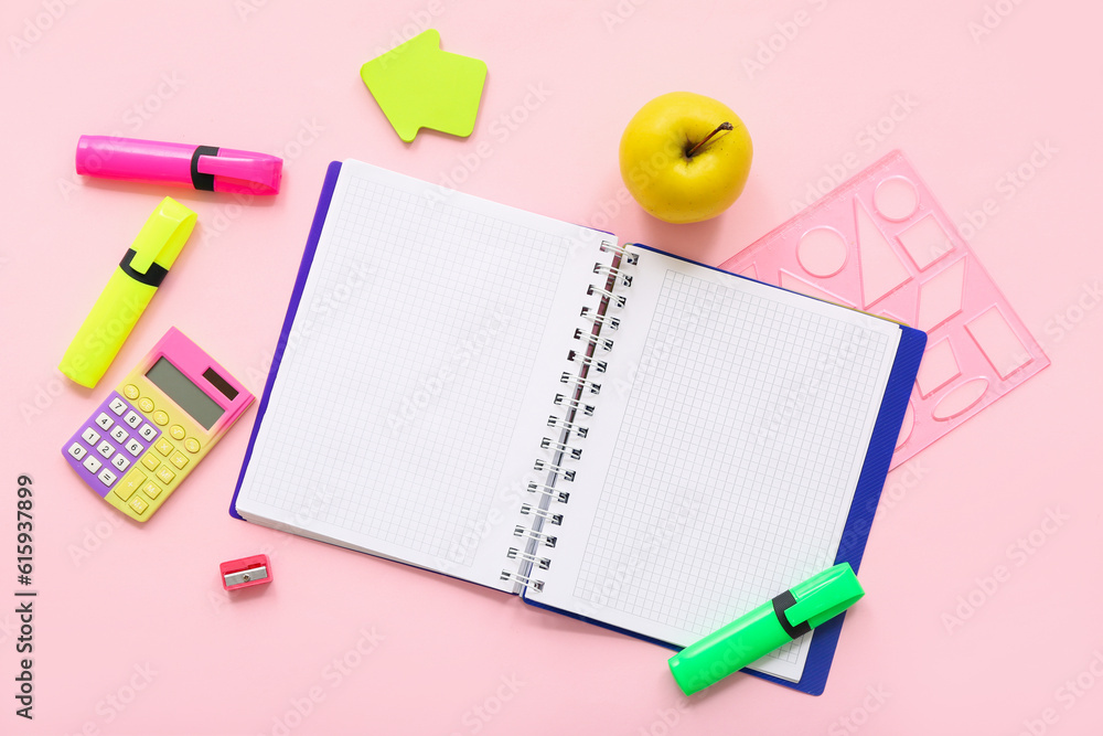 Open notebook with fresh apple, calculator and different stationery on pink background