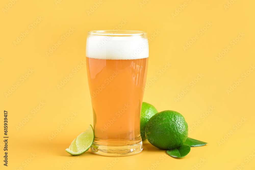 Glass of cold beer with lime on yellow background