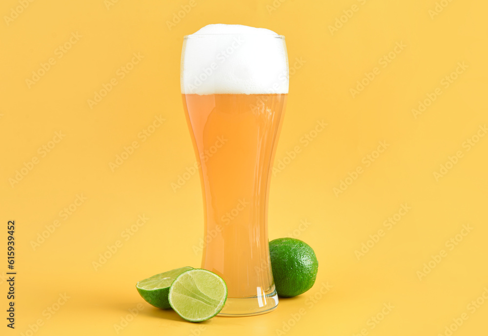 Glass of cold beer with lime on yellow background