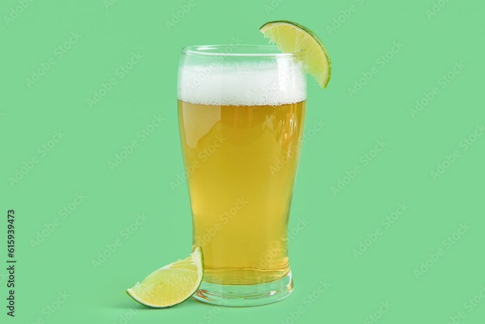 Glass of cold beer with lime on green background