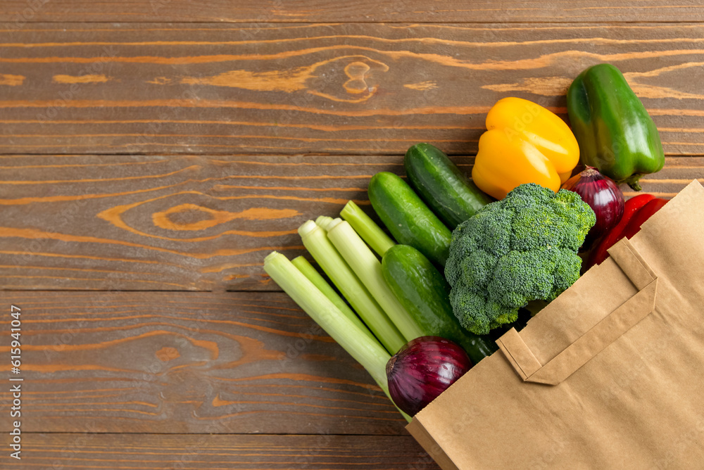 Paper bag with different vegetables on wooden background