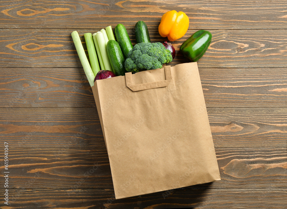 Paper bag with different vegetables on wooden background