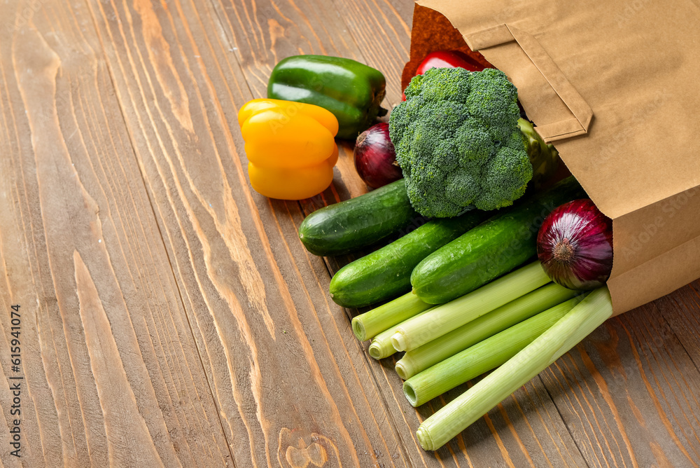 Paper bag with different vegetables on wooden background