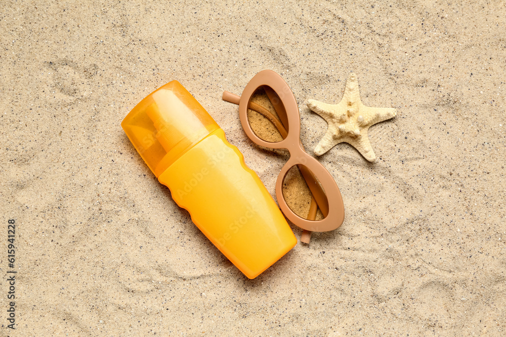 Sunglasses with bottle of sunscreen cream and starfish on sand