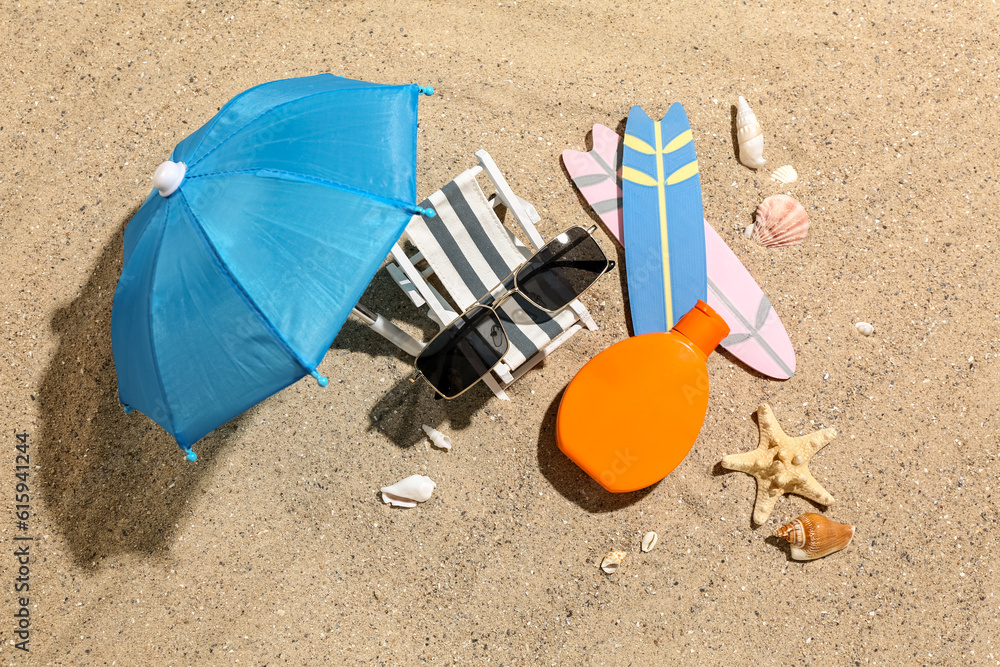 Creative composition with sunglasses, bottle of sunscreen cream, mini deckchair and surfboards on sa