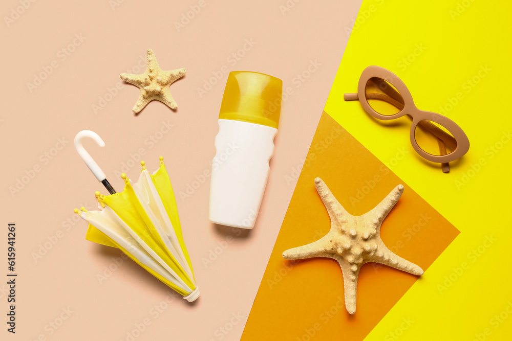 Sunglasses with starfishes, mini umbrella and bottle of sunscreen cream on color background