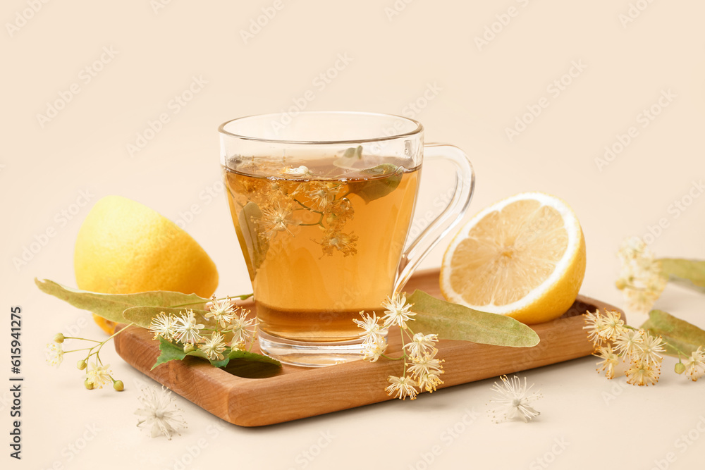 Board with glass cup of linden tea and lemon on beige background