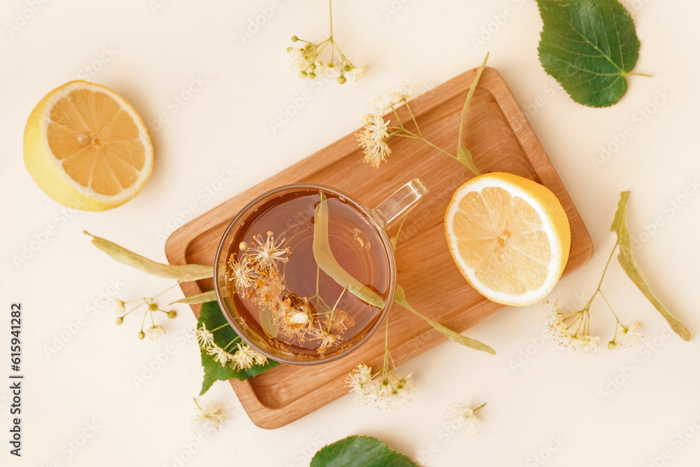 Board with glass cup of linden tea and lemon on beige background