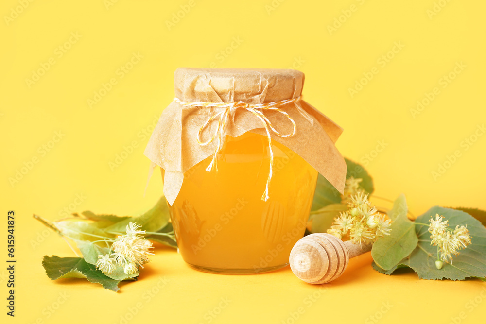 Glass jar with linden honey and dipper on yellow background