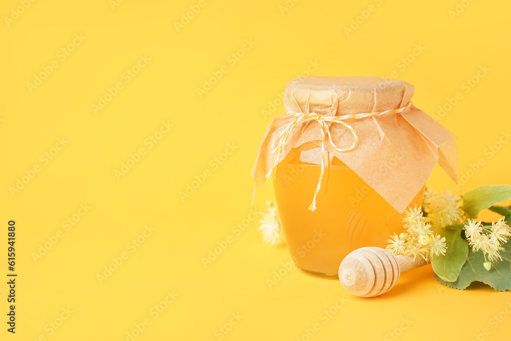 Glass jar with linden honey and dipper on yellow background