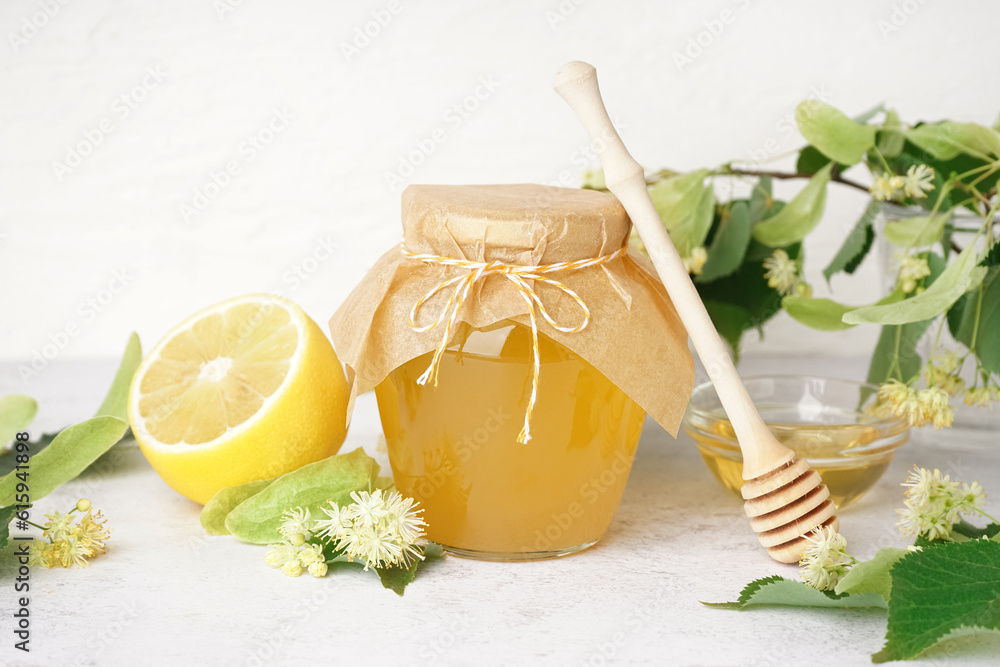 Glass jar of linden honey, dipper and fresh linden flowers on light background