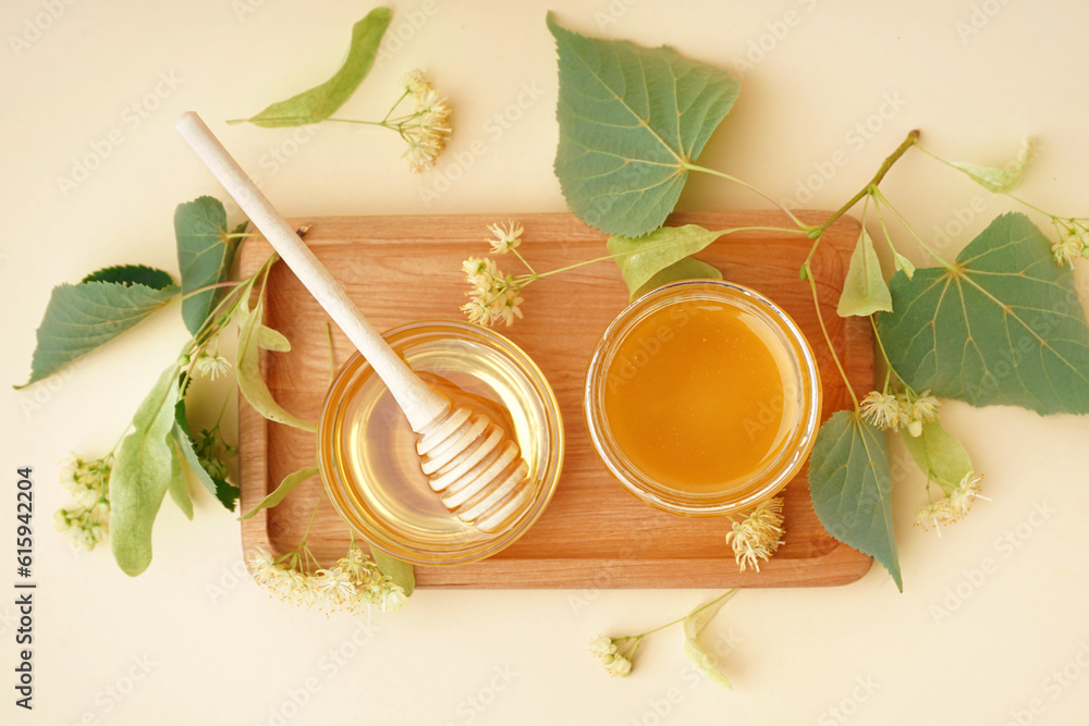 Wooden board with glass bowl and jar of linden honey on light background