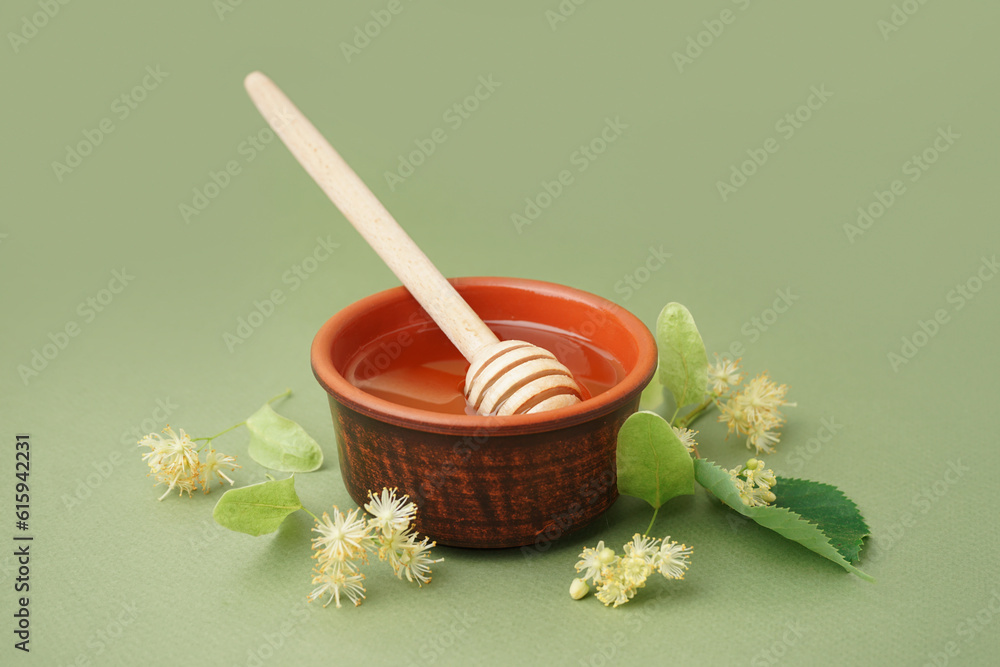 Bowl with linden honey and dipper on green background