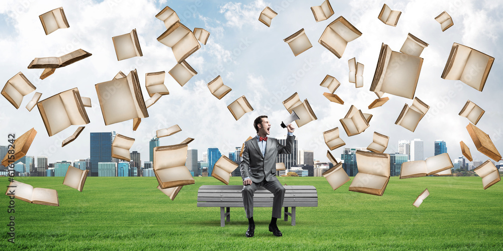 Businessman in summer park announcing something in loudspeaker and books falling from above