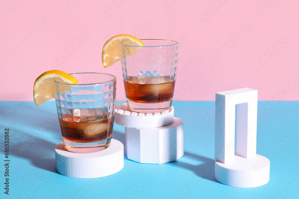 Glasses of rum with ice cubes, lemon slices and plaster figures on colorful background