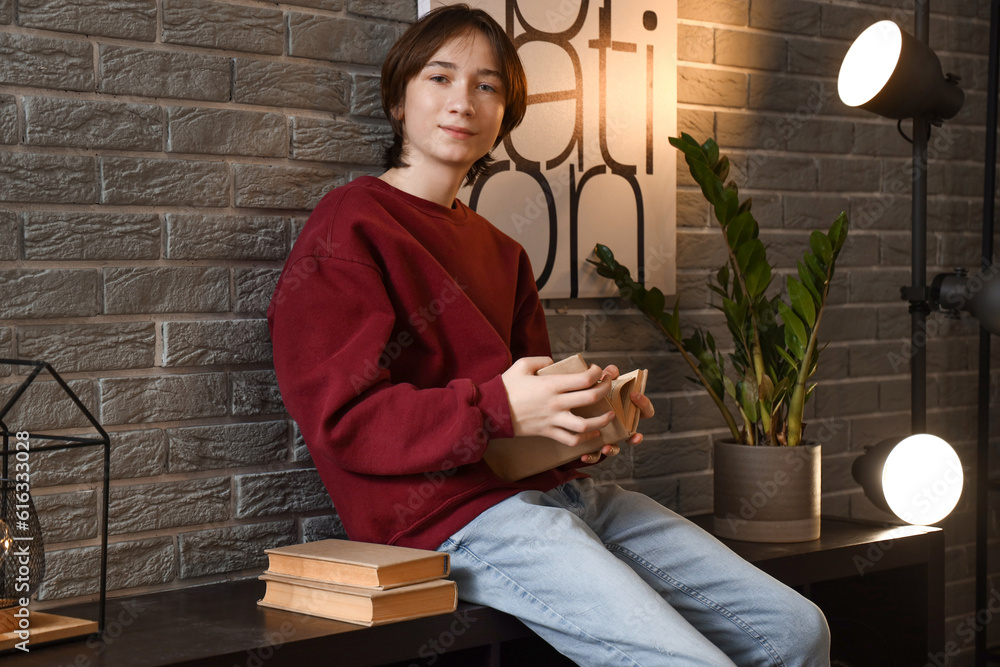 Teenage boy reading book at home late in evening