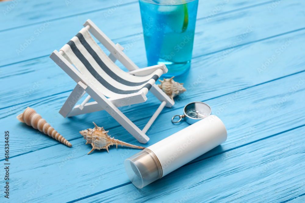 Composition with miniature deck chair, bottle of sunscreen and compass blue wooden background