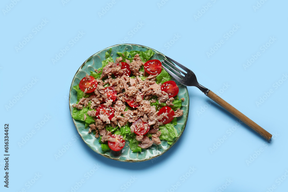 Plate with delicious tuna salad and fork on blue background