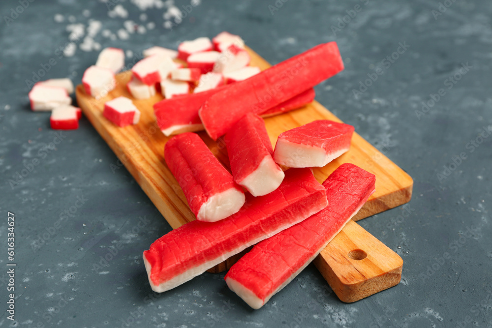 Wooden board with tasty crab sticks on green background