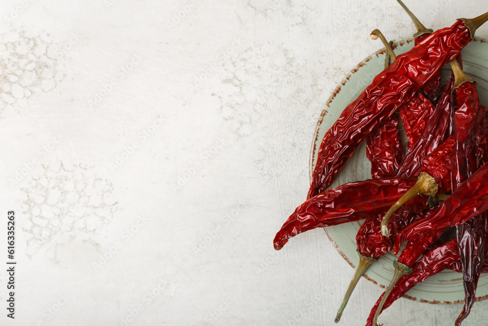 Plate with dry hot chili peppers on light background