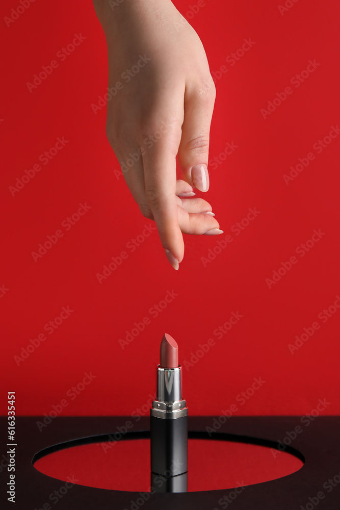 Female hand and lipstick on red background