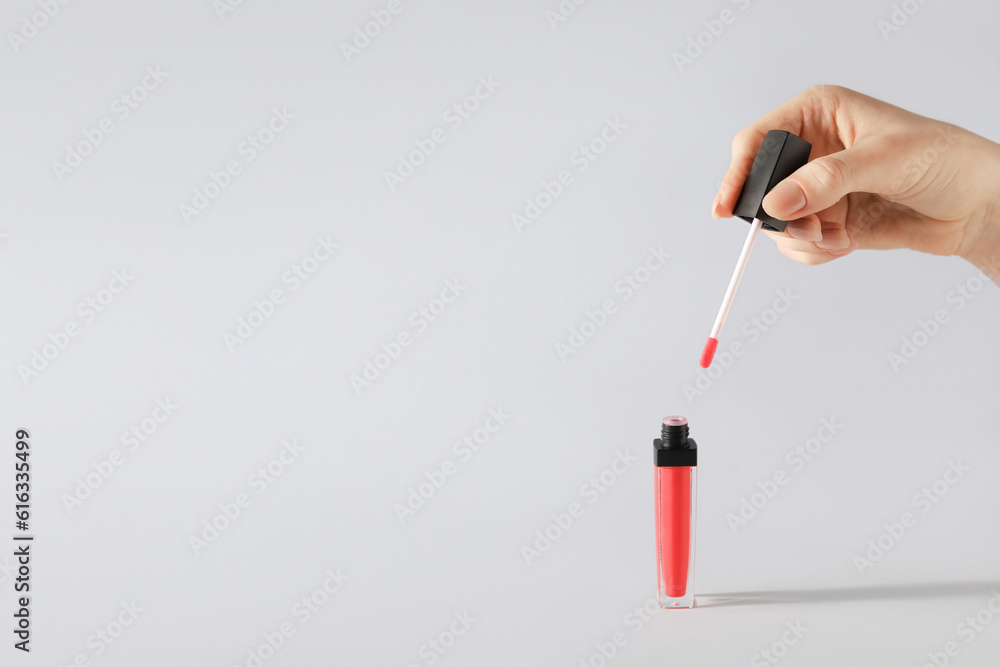 Female hand and lip gloss on white background