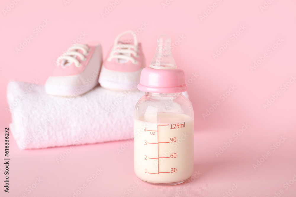 Bottle of milk for baby and accessories on pink background