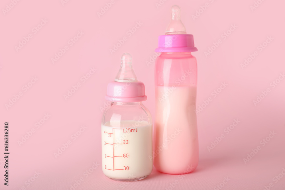 Bottles of milk for baby on pink background