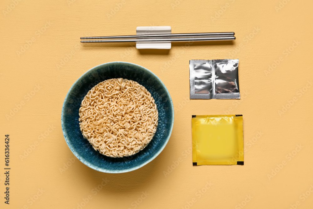 Raw instant noodles in bowl with chopsticks and seasoning yellow background