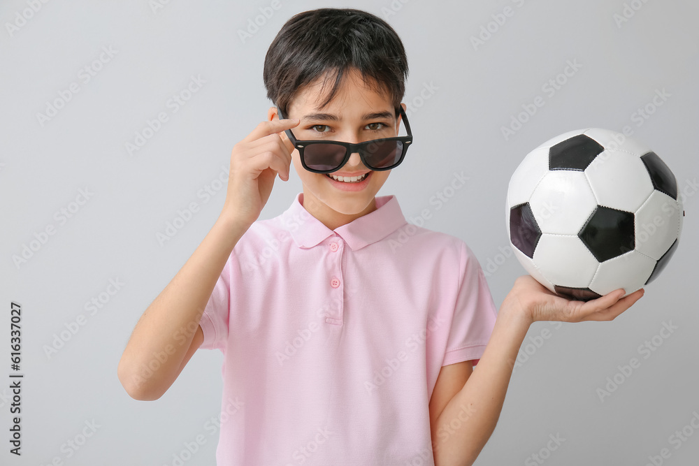 Little boy with soccer ball wearing sunglasses on grey background