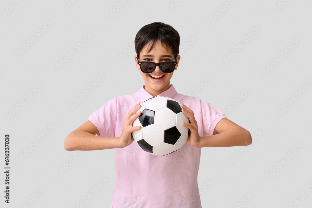 Little boy with soccer ball wearing sunglasses on grey background