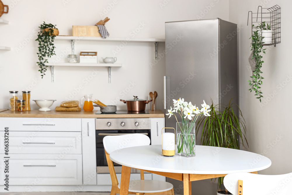 Interior of light kitchen with stylish fridge, counters, shelves, table and chairs