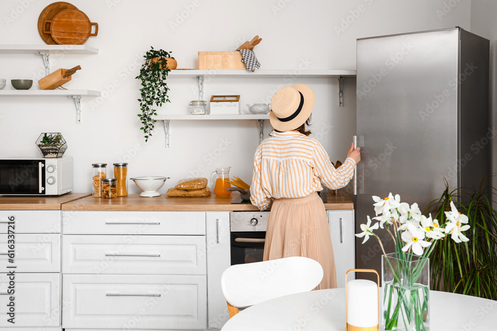 Young woman opening stylish fridge in kitchen