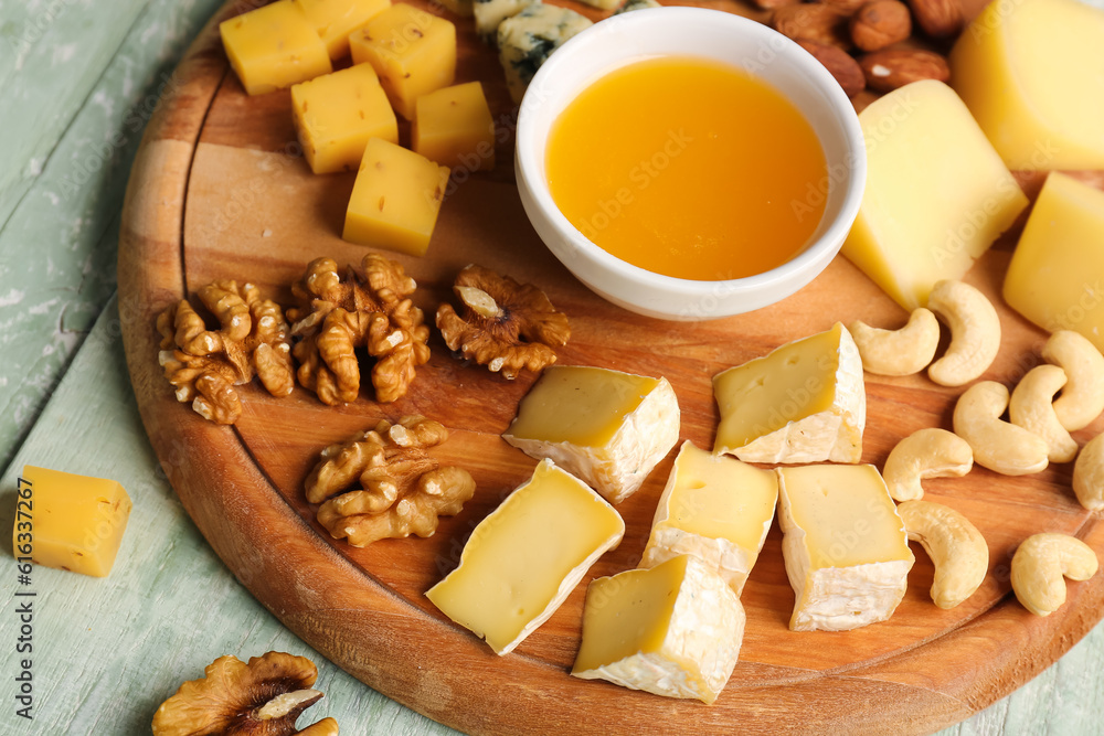 Wooden board with pieces of tasty cheese, nuts and honey on table, closeup