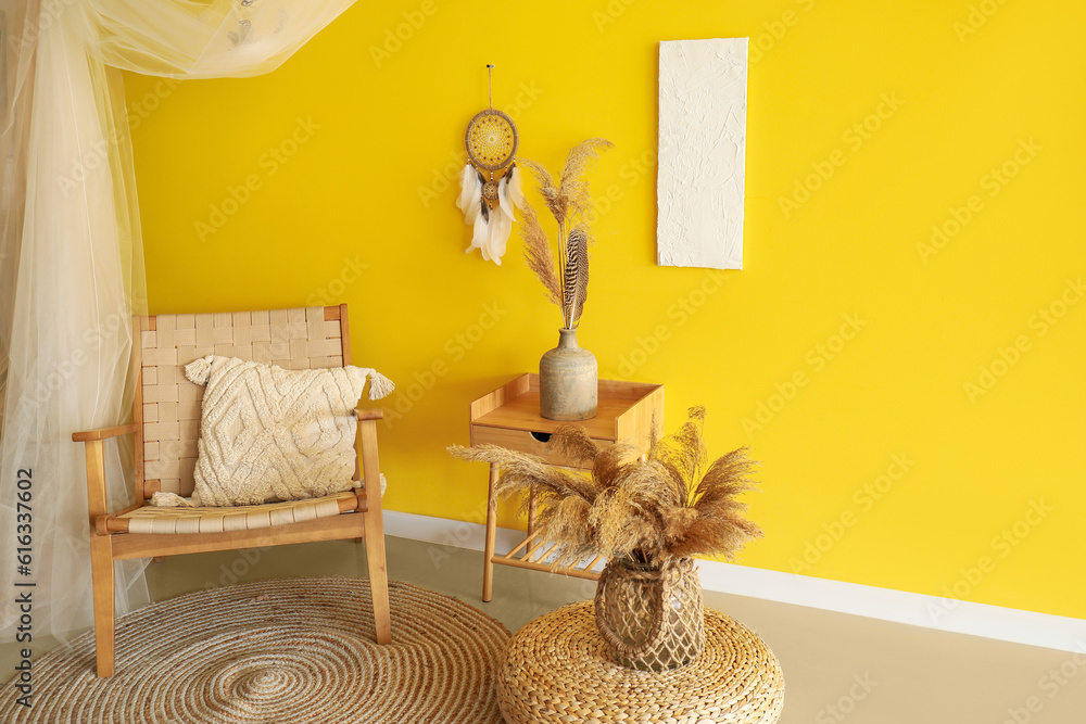 Interior of modern living room with armchair, table and dream catcher hanging on yellow wall